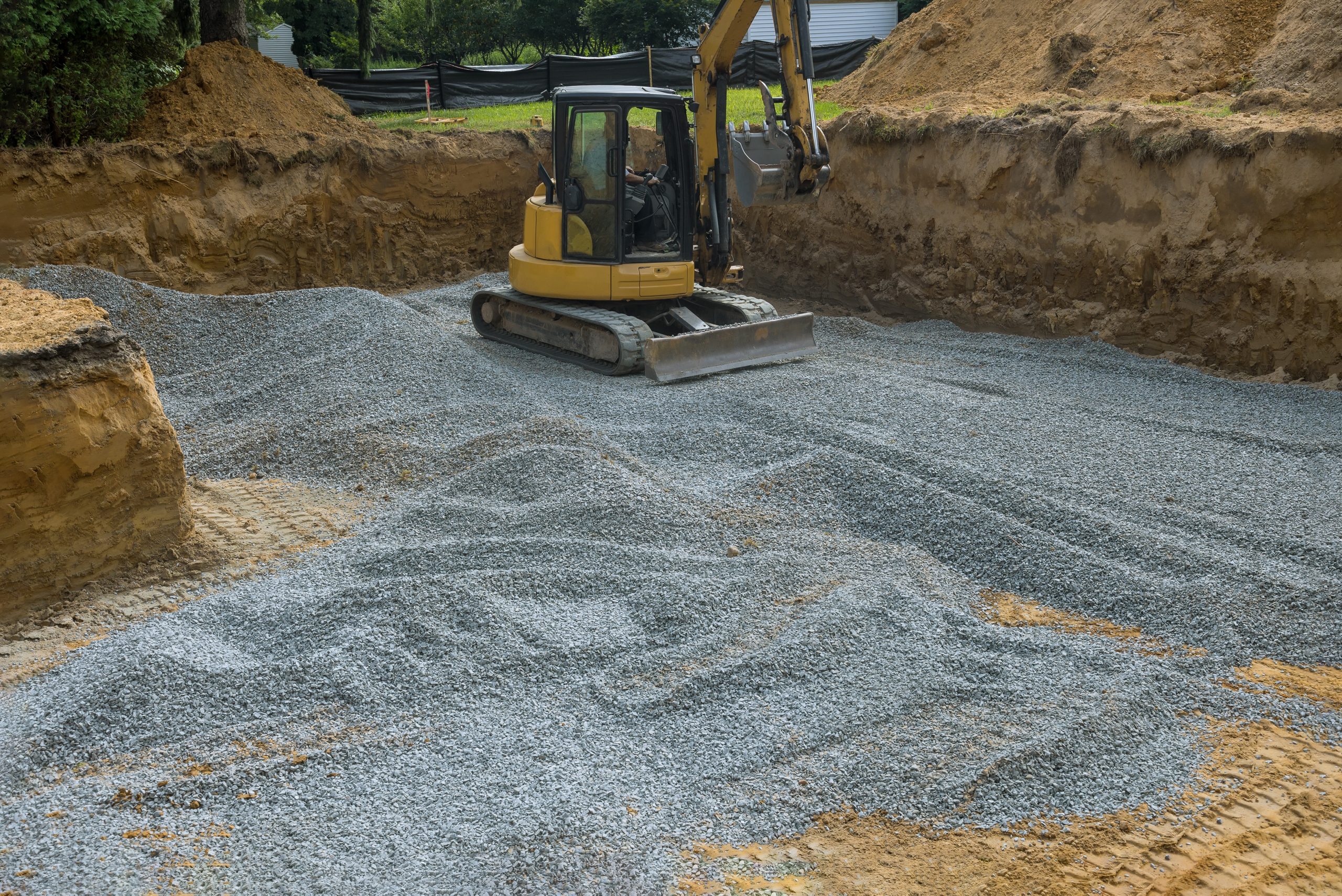 Excavator with a bucket lowered down on gravel stones for construction of foundation