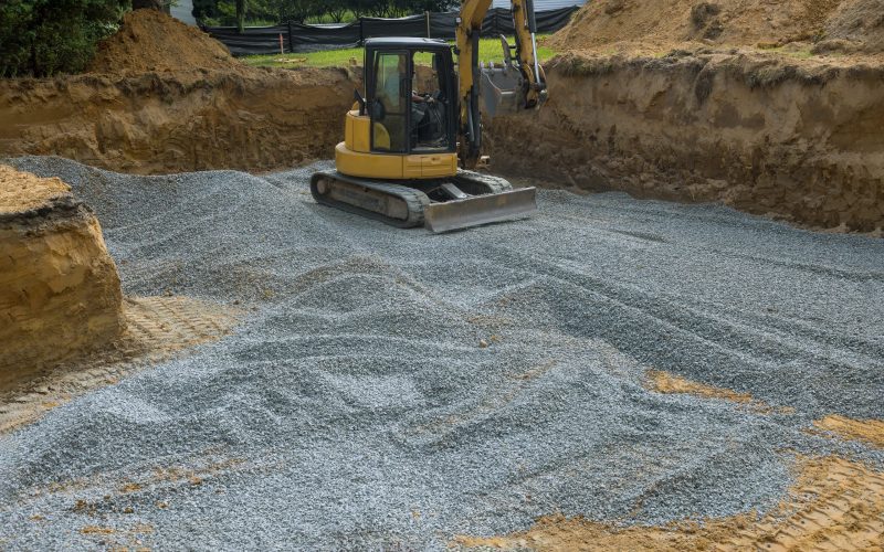Excavator with a bucket lowered down on gravel stones for construction of foundation